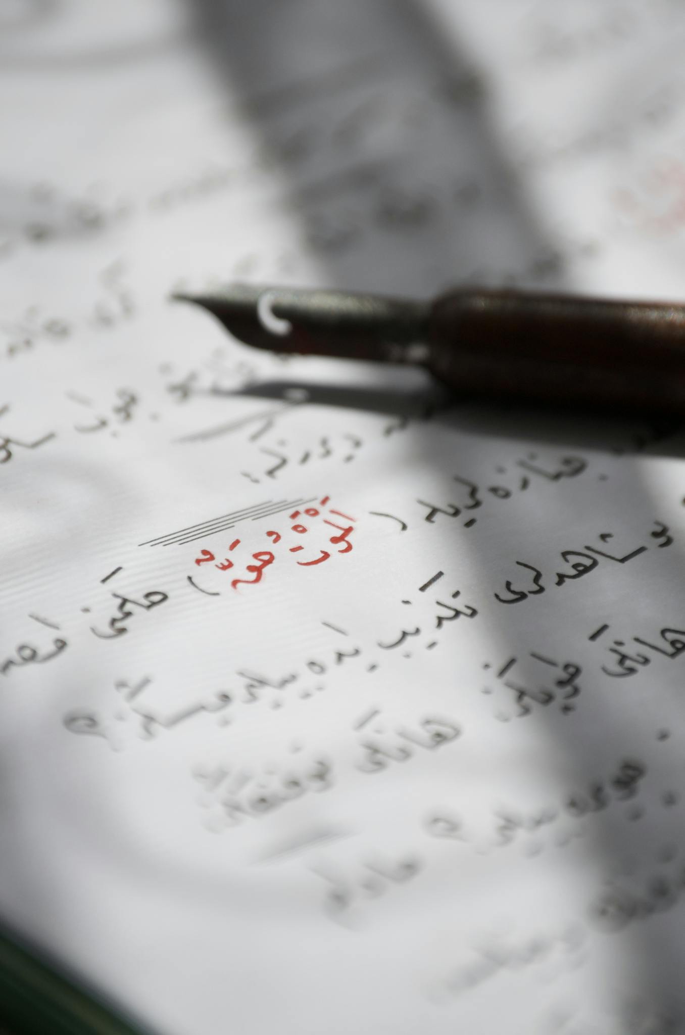 Close-up of a fountain pen on a page with Arabic calligraphy in soft light.